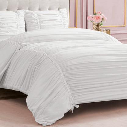 A neatly made bed showcases the Ribbon Ruched Comforter Set with matching pillows against a pink, gold-accented wall. A vase of pink roses rests on a small bedside table.