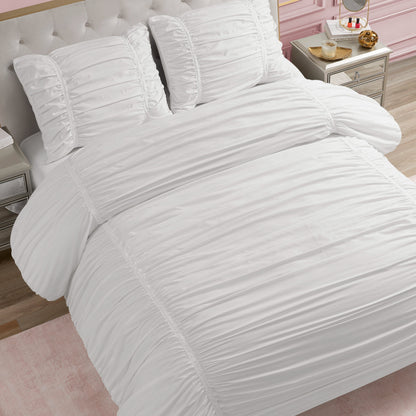 A neatly made bed features the Ribbon Ruched Comforter Set with matching pillows, set in a bedroom with light wood floors, a pink accent rug, and nightstands. Subtle ribbon ruching adds an elegant touch to the cozy space.