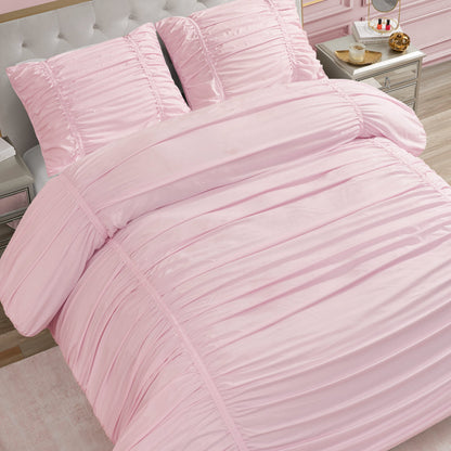 A neatly made bed featuring the Ribbon Ruched Comforter Set in light pink with matching pillows, placed in a bedroom with light furniture and a silver nightstand displaying a tray with a teapot, cup, and pastries.