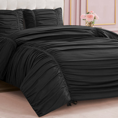 A neatly made bed features the Ribbon Ruched Comforter Set in black with matching pillows, accented by elegant ribbon detailing. Pink walls with decorative molding and a vase of pink roses on the bedside table complete the chic look.