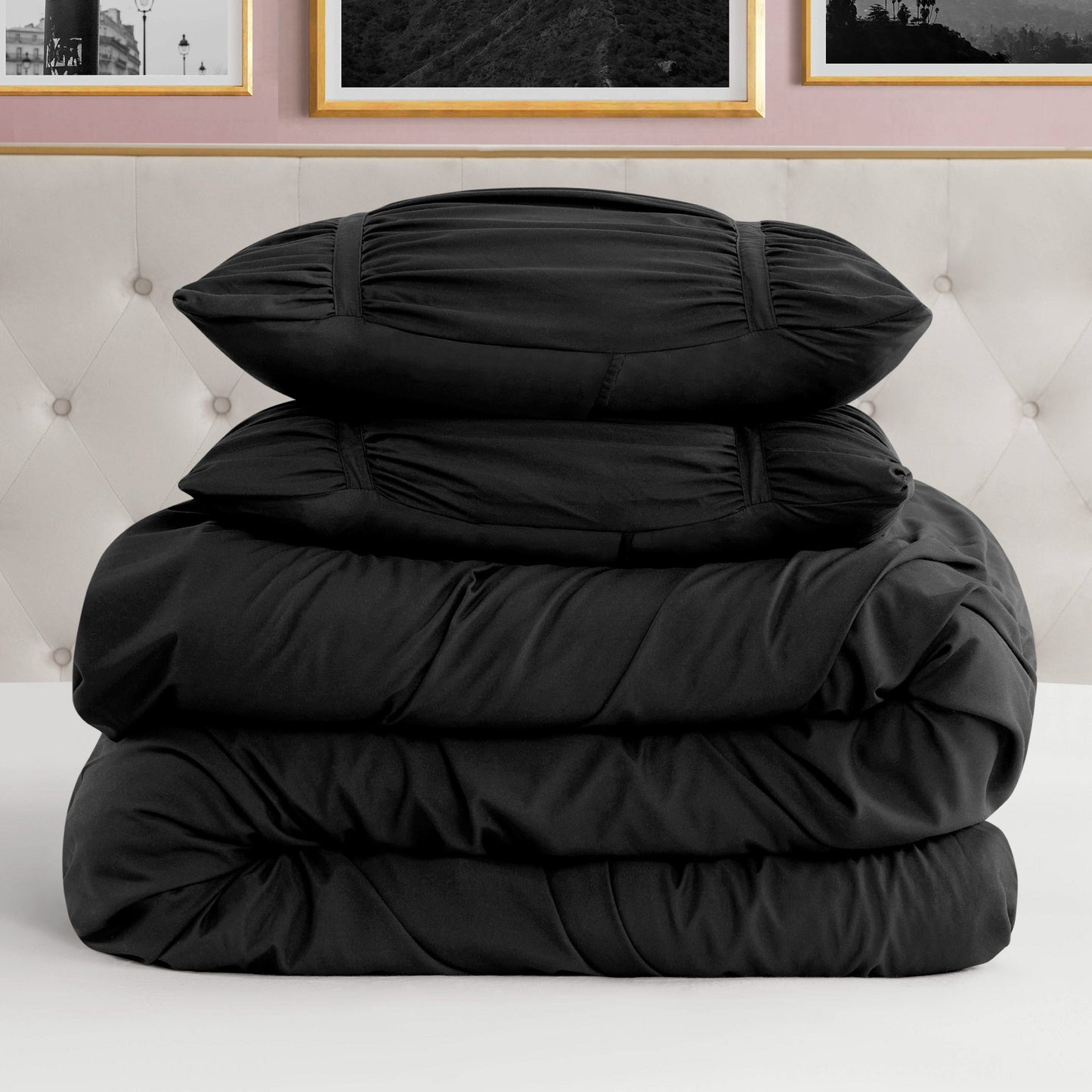 A neatly folded Ribbon Ruched Comforter Set with two matching pillow shams stacked on a white bed, set against a tufted beige headboard and framed pictures on a pink wall.