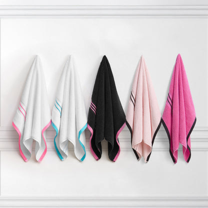 Five Neon Border Bath Towels hang on a white wall: white with pink trim, white with blue trim, black with pink trim, light pink with dark trim, and bright pink with dark trim.