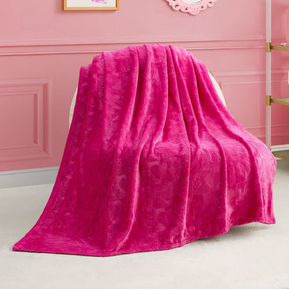 A Plush Throw Blanket in bright pink is draped over a white chair in a pink room with decorative wall molding and gold shelves.