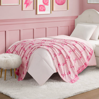 A neatly made bed with a Plush Throw Blanket featuring pink bows, in a pink-themed bedroom with framed art, a white upholstered headboard, a white furry stool, and a white rug.