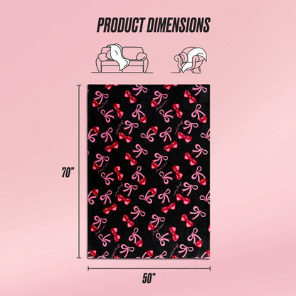 The Sweet Cherry Bows Plush Throw Blanket, in black with pink and red bow patterns, is shown on a pink background. Sized 70" x 50", this ultra-soft Juicy Couture throw is perfect for your couch or bed. Product dimensions are highlighted.