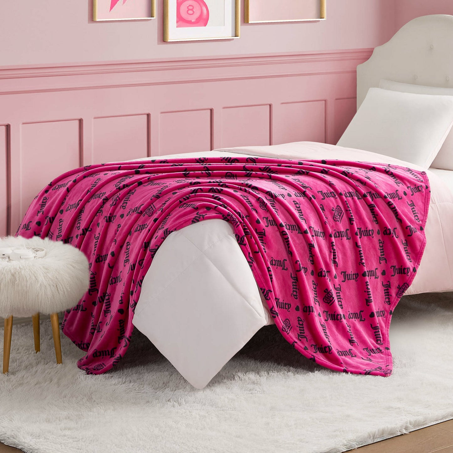 A Plush Throw Blanket with black script text drapes over a neatly made bed in a pink-themed bedroom featuring white furniture, a fluffy white rug, and framed artwork on the wall.