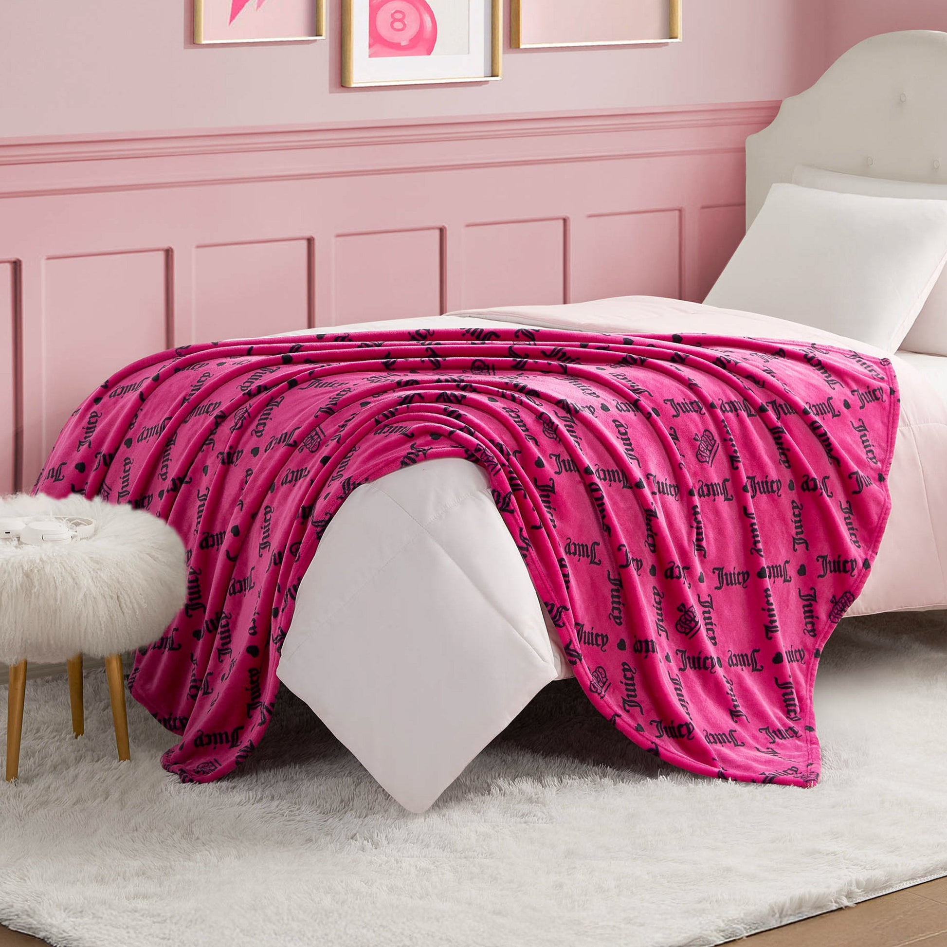 A Plush Throw Blanket with black script text drapes over a neatly made bed in a pink-themed bedroom featuring white furniture, a fluffy white rug, and framed artwork on the wall.