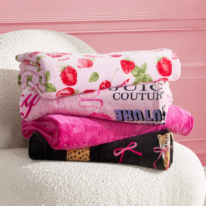 Three folded Plush Throw Blankets sit on a textured white chair: the top is white with strawberry prints, the middle is bright pink with bold text, and the bottom features black leopard spots and pink bow designs.