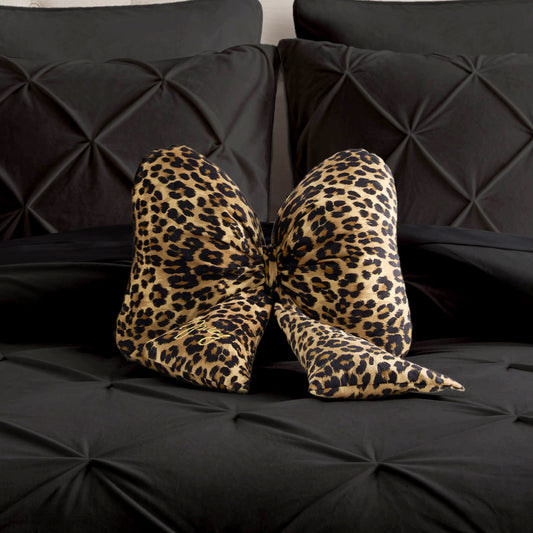 A Bow Shaped Decorative Pillow with a leopard print pattern is placed on a bed featuring black, textured bedding and pillows.