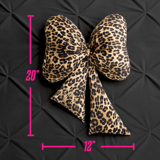 The Bow Shaped Decorative Pillow, featuring a large leopard print design and measuring 20 inches tall by 12 inches wide, is displayed against a black textured background. Pink lines and numbers highlight the dimensions of this decorative bow pillow.
