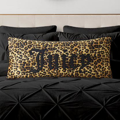 A Gothic Cheetah Decorative Pillow featuring a bold leopard print and the word "Juicy" in striking black script sits on a black, tufted bed with black bedding and a light-colored headboard, adding a chic touch to the décor.