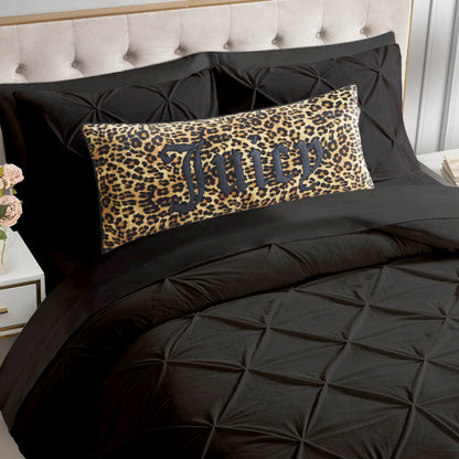 A bed with a tufted beige headboard, black bedding, and a rectangular Gothic Cheetah Decorative Pillow featuring leopard print and the word "Juicy" in bold black letters. A bedside table with pink roses is visible on the left.