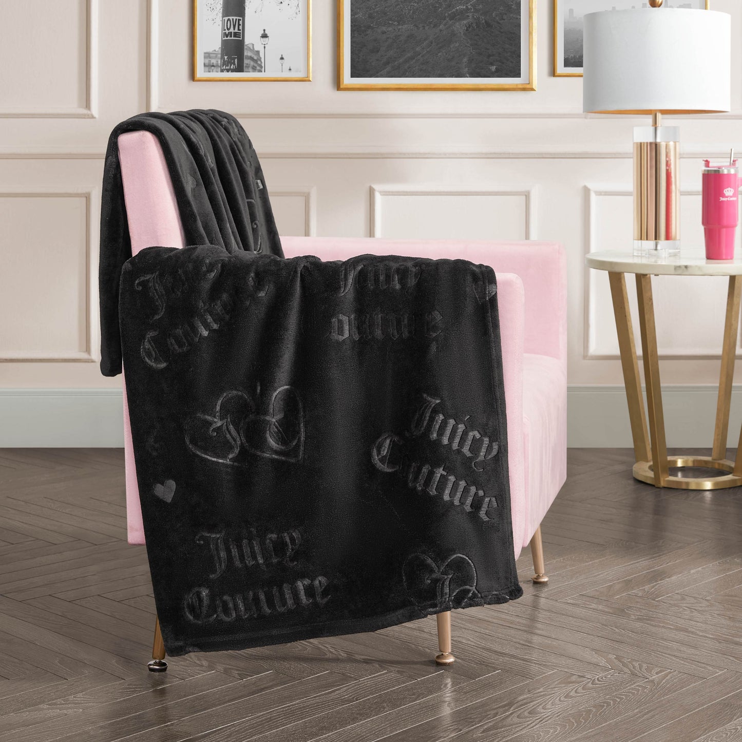 An Embossed Plush Throw Blanket with heart designs is draped over a pale pink armchair in a chic room featuring framed art, a white lamp, and a round side table.