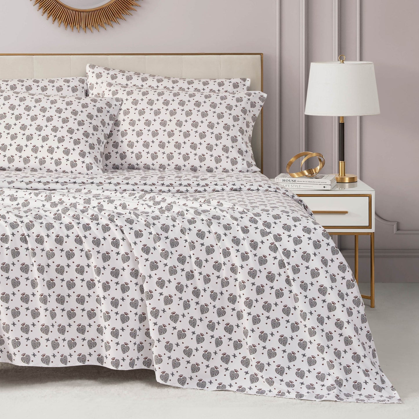 A stylish, light gray bedroom features a neatly made bed with a white and brown floral comforter, luxury pillows, and the Microfiber Sheet Set With Extra Pillowcases beside a white and gold nightstand holding books, gold decor, and a modern lamp.
