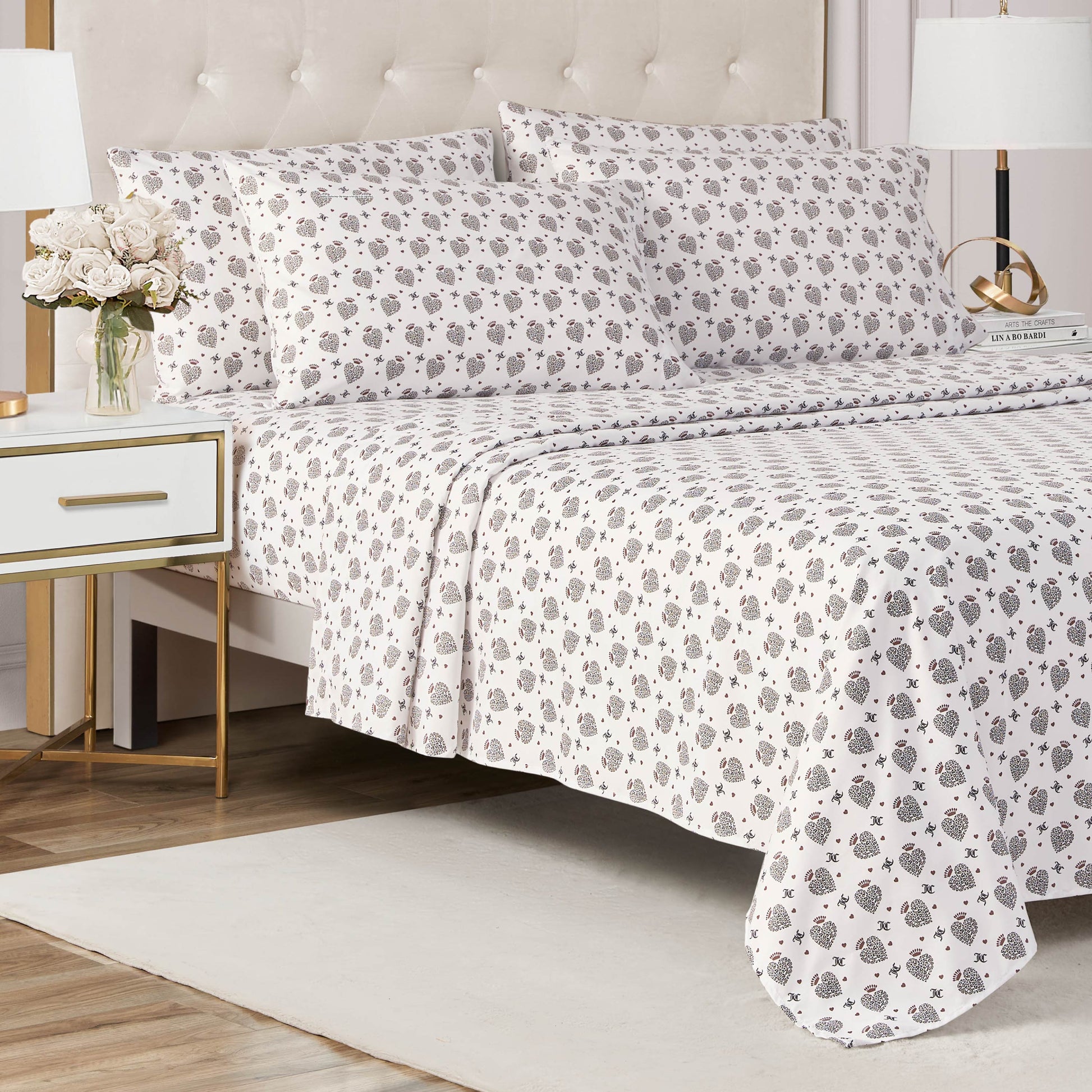 A neatly made bed with the Microfiber Sheet Set With Extra Pillowcases—white sheets and pillowcases adorned with a gray and black floral pattern—stands beside a white nightstand holding a vase of flowers in a bright, modern bedroom.