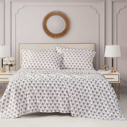 A neatly made bed features the Microfiber Sheet Set With Extra Pillowcases in white and gray floral, flanked by white nightstands with lamps, in an elegant room with mauve walls and a round gold-framed mirror above the bed.