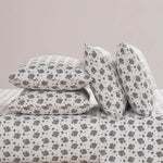 A neatly made bed features the Microfiber Sheet Set With Extra Pillowcases, showcasing white bedding adorned with a repeating pattern of small black and gray hedgehogs and tiny red hearts on all pillows.