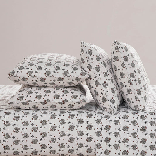 A neatly made bed features the Microfiber Sheet Set With Extra Pillowcases, showcasing white bedding adorned with a repeating pattern of small black and gray hedgehogs and tiny red hearts on all pillows.