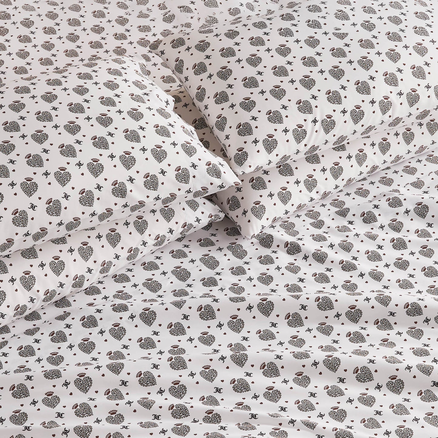 Close-up of a bed with white sheets and pillowcases featuring a small, dark floral and geometric pattern. The Microfiber Sheet Set With Extra Pillowcases offers luxury bedding that looks soft, neat, and elegantly arranged.