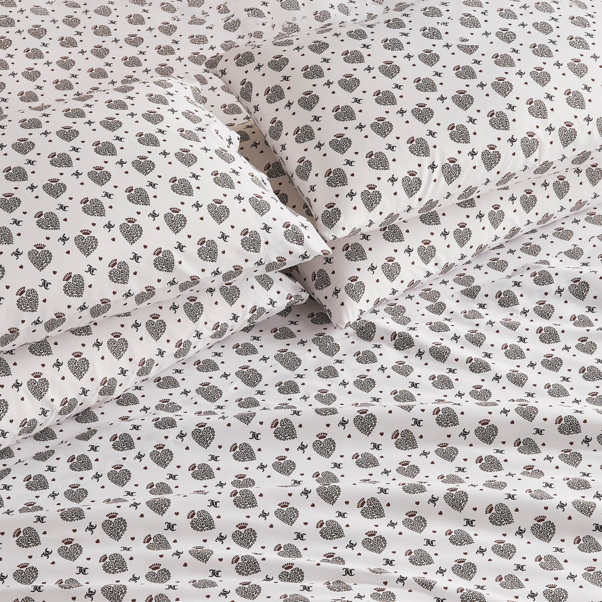 Close-up of a bed with white sheets and pillowcases featuring a small, dark floral and geometric pattern. The Microfiber Sheet Set With Extra Pillowcases offers luxury bedding that looks soft, neat, and elegantly arranged.