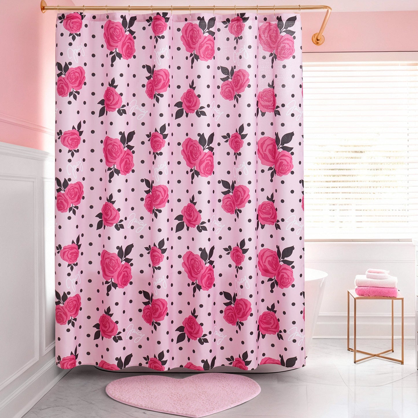 A pink bathroom with a Shower Curtain and Hooks Set featuring red roses and black polka dots, a pink heart-shaped rug, white tub, folded towels on a stool, and a window with white blinds.