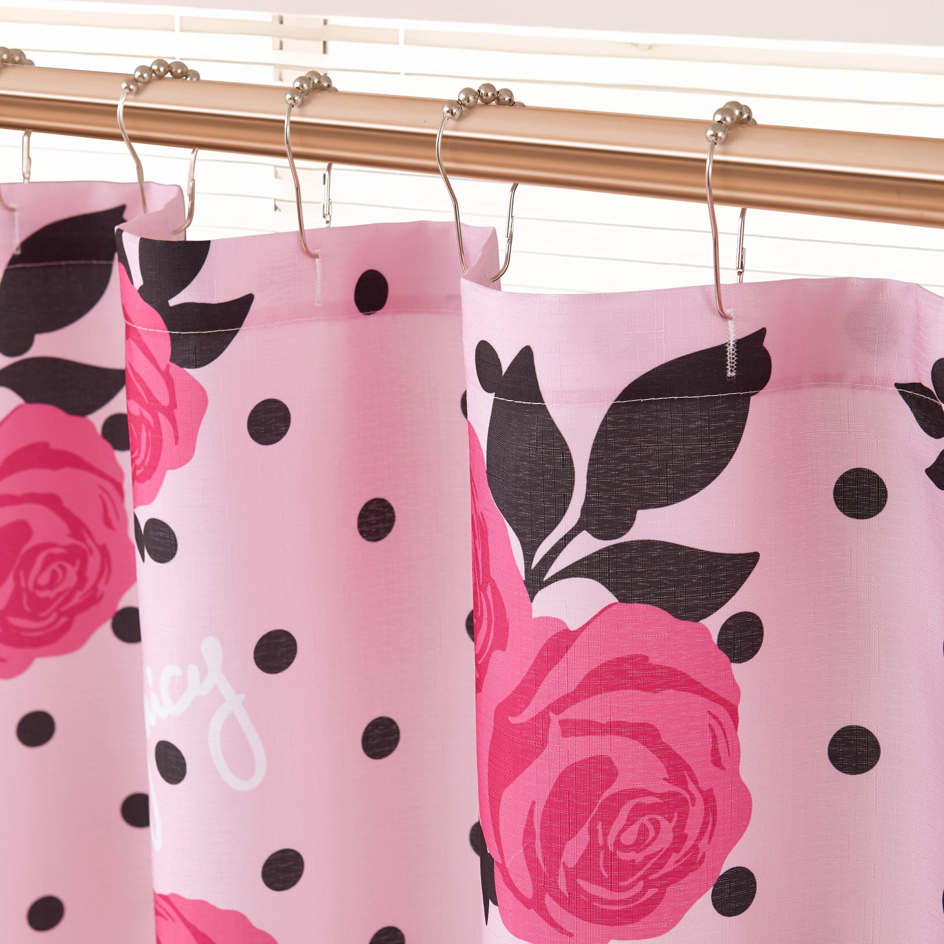 Close-up of the Shower Curtain and Hooks Set featuring black polka dots and large red rose patterns, hanging from a gold rod with round hooks in front of white window blinds.