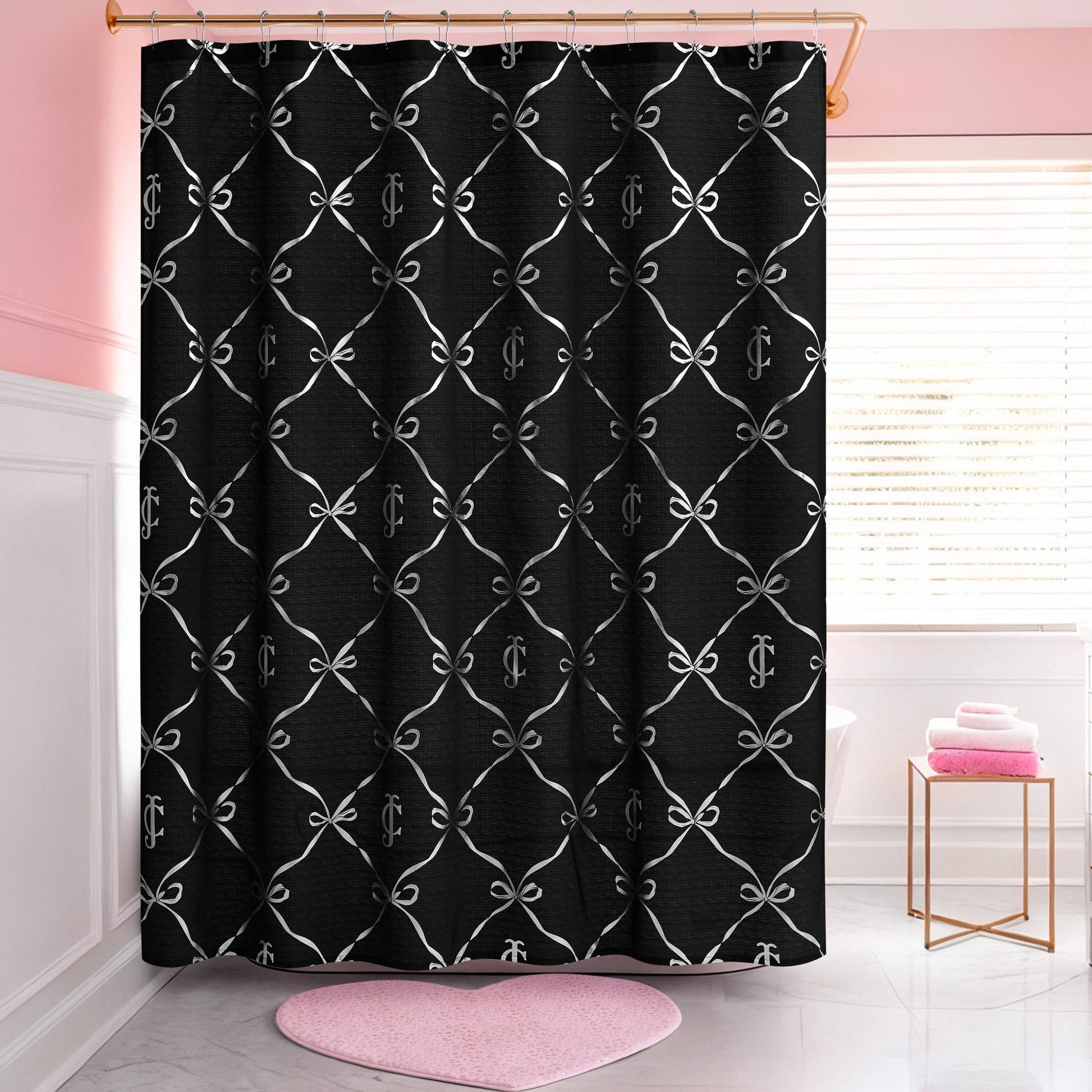 A pink and white bathroom features a Shower Curtain and Hooks Set with a white bow and monogram print, a pink heart-shaped rug, folded towels, and a window that lets in natural light.