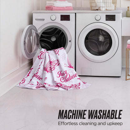 A white and pink shower curtain from the Juicy Couture Shower Curtain and Hooks Set hangs partly in and out of a front-loading washer, next to a dryer. Text: MACHINE WASHABLE—Effortless cleaning, just like your favorite Juicy Couture set.