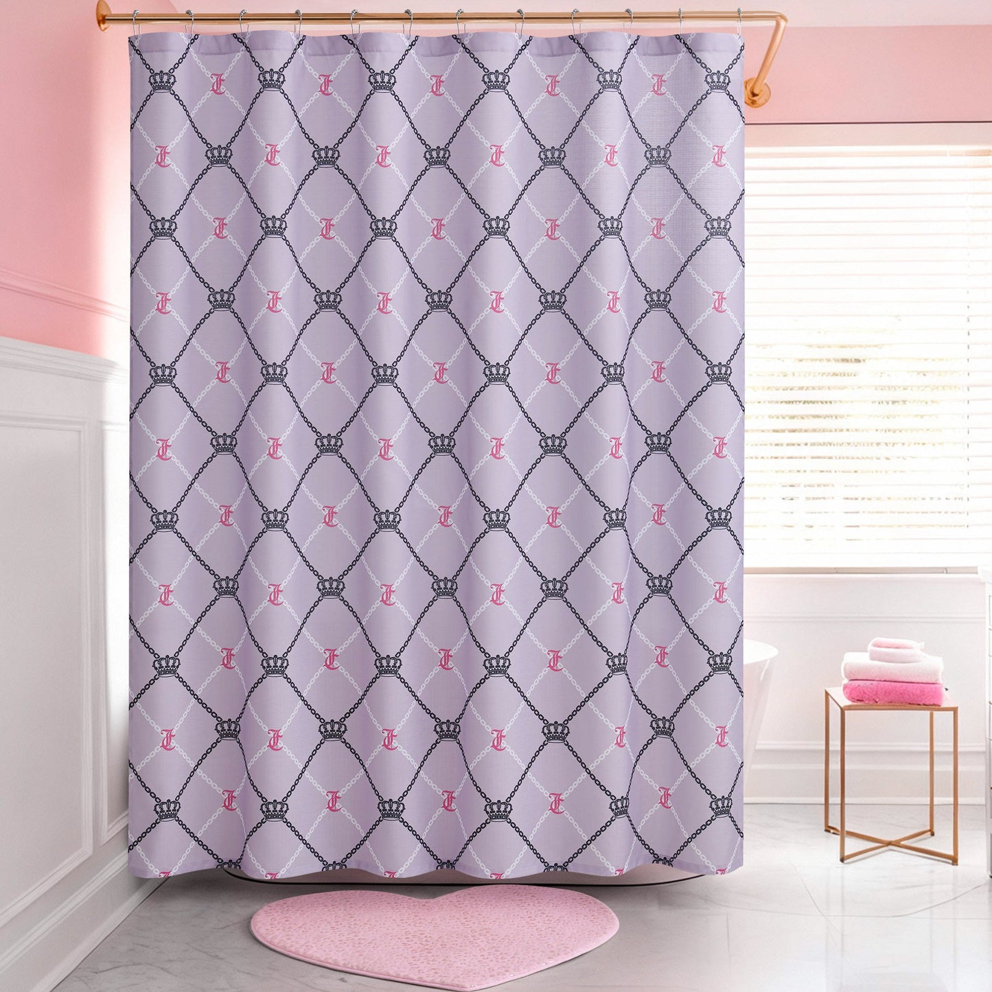 A bathroom with pink and white walls features a Shower Curtain and Hooks Set decorated with crowns and pink script. The room also has a white tub, a window with blinds, and neatly stacked pink towels near the tub.