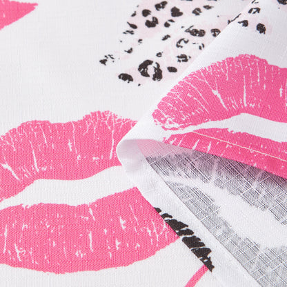 A close-up of the Cheetah Kisses Shower Curtain with PEVA Liner and Hooks 14-Piece Set showcases white fabric adorned with vibrant pink lip prints and black leopard spots, including a folded corner that reveals the reverse side—making it the perfect bold statement piece for your bathroom decor.
