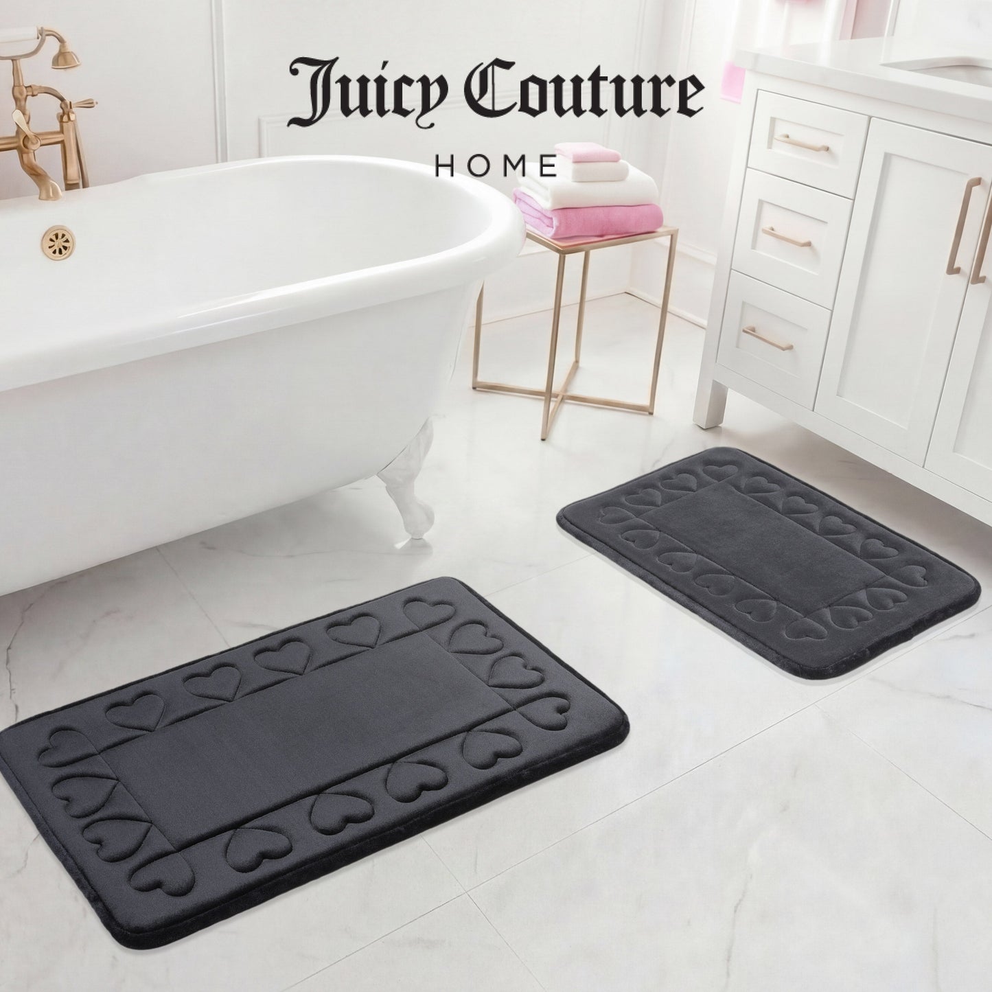 Two dark gray Quilted Memory Foam Bath Mats from Juicy Couture rest on a white marble floor near a clawfoot tub and vanity, adding luxury to the space. Juicy Couture Home is written at the top of the image.