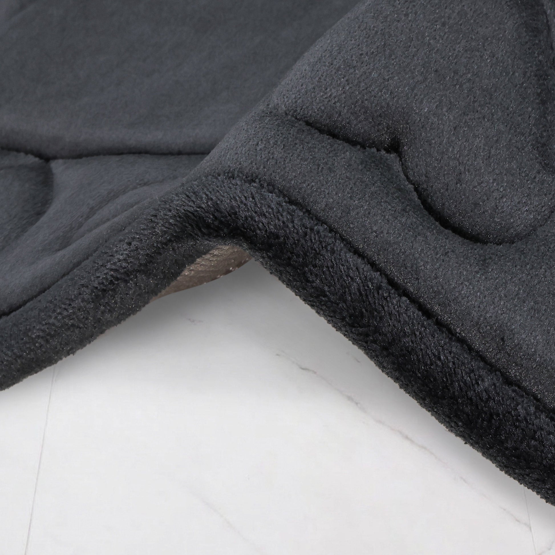 A close-up of a dark gray Quilted Memory Foam Bath Mat from a 2-piece set, draped over a light surface, highlighting its plush, soft texture and curved edge.