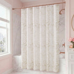 A bathroom with marble walls and a window features the Stassi Shower Curtain with PEVA Liner and Hooks 14-Piece Set in a stylish white and beige pattern, making a striking statement in the space. A vanity adorned with pink flowers in a vase and a round mirror on the right side enhances the elegant bath decor.