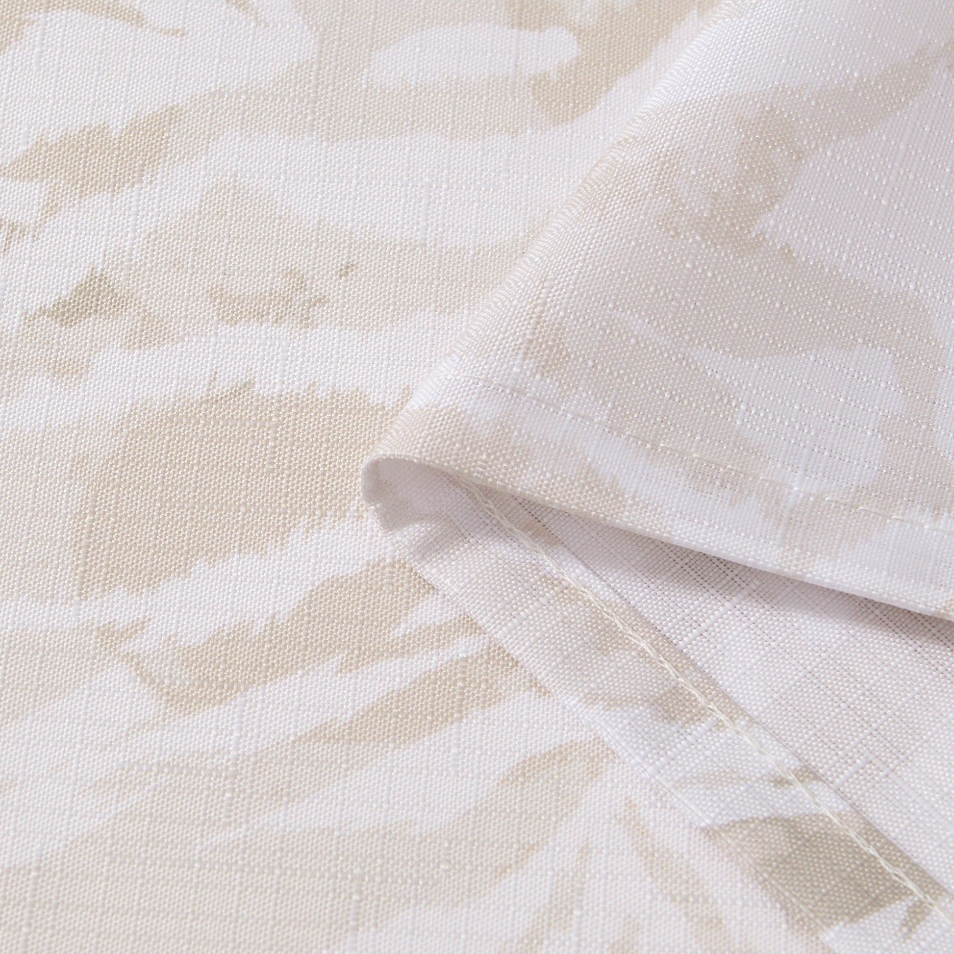 Close-up of the Stassi Shower Curtain with PEVA Liner and Hooks 14-Piece Set, featuring beige and white fabric with a subtle abstract pattern. The fabric is folded to highlight its texture and neatly stitched edges—perfect for elevating your bath decor or making a statement in your bathroom ensemble.