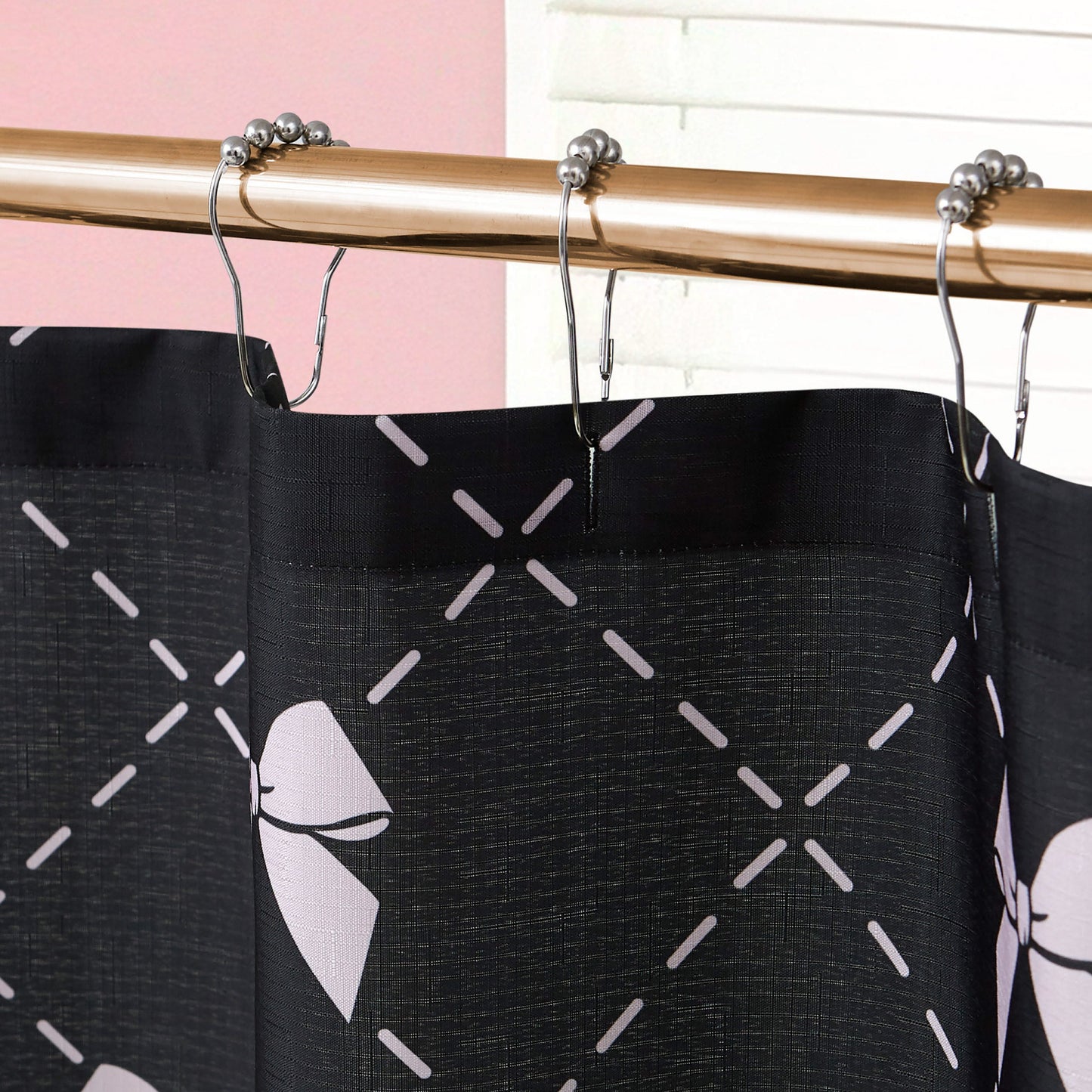 A close-up of the Shower Curtain and Hooks Set featuring a pink bow and crisscross pattern, hanging from metal hooks. This fabric curtain adds a chic accent to your bathroom, shown with a pink wall and white blinds in the background.