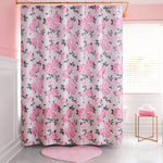 A pink and white bathroom features a Shower Curtain and Hooks Set with a pink rose floral pattern, a pink heart-shaped bath mat, and a stack of pink towels on a white stool by the window—stylish decor for any space.