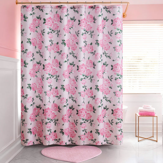 A pink and white bathroom features a Shower Curtain and Hooks Set with a pink rose floral pattern, a pink heart-shaped bath mat, and a stack of pink towels on a white stool by the window—stylish decor for any space.