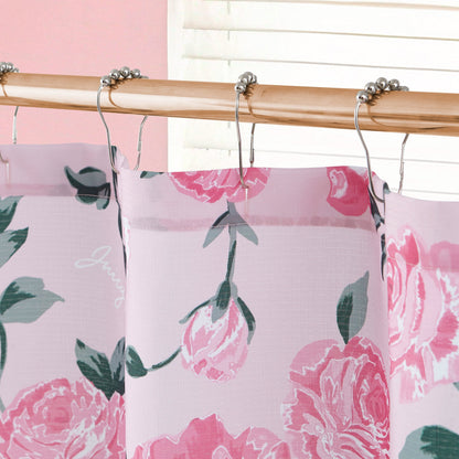 A close-up of the Shower Curtain and Hooks Set featuring pink florals and green leaves hangs on a bamboo rod with metal hooks, complemented by blinds and a light pink wall for a charming bathroom backdrop.