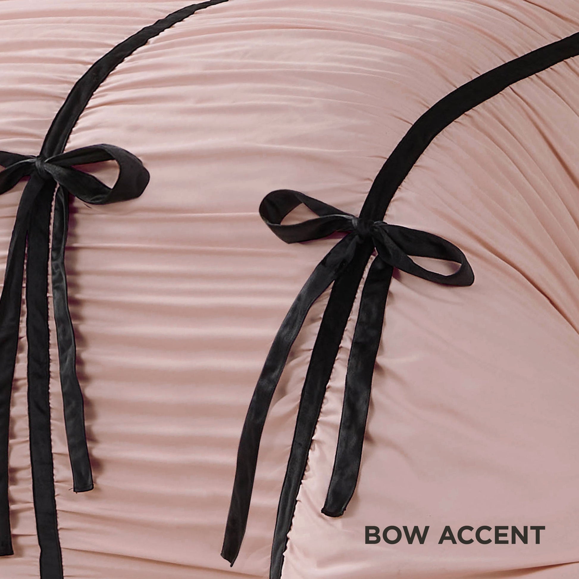 Close-up of pale pink ruched fabric with two velvet bows and black trim from the Amelie Bows Ruched Comforter Set. “BOW ACCENT” appears in the bottom right corner.