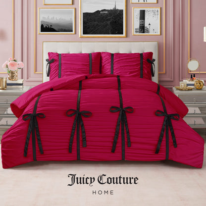 A neatly made bed with the Amelie Bows Ruched Comforter Set in bright pink and chic bedding with black velvet bows. The room features light pink walls, framed photos, a gray headboard, and a mirrored dresser topped with flowers.