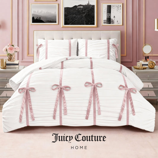 The Amelie Bows Ruched Comforter Set by Juicy Couture, featuring pink velvet bows and matching pillows, adds style to a pink-themed bedroom. The ultra-soft comforter displays the Juicy Couture Home logo at the bottom.
