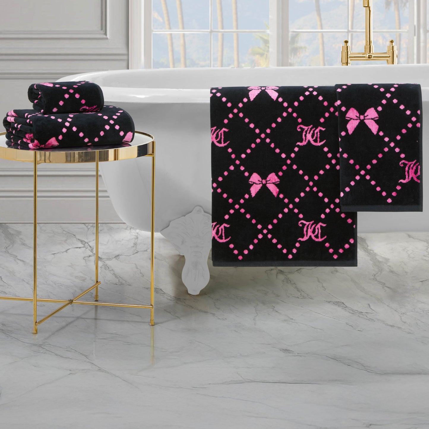 The Printed Jacquard Bath Towel Set, featuring pink bows and dotted diamond patterns, is showcased in a luxurious bathroom with a white bathtub, marble flooring, and a gold side table.