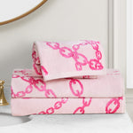 Two Printed Jacquard Bath Towel Set towels, featuring light pink with bold chain-link designs, are neatly folded and stacked on a white marble bathroom countertop beside a gold faucet.