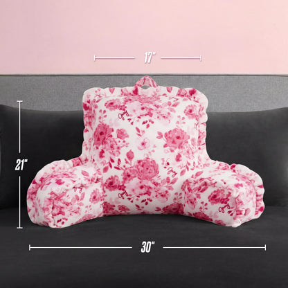 A white and pink floral-patterned Backrest Pillow with armrests is on a dark gray couch. Its overlaid dimensions are 17" tall, 21" high, and 30" wide. The background wall is light pink.