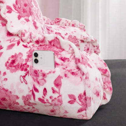 A white smartphone sits in the side pocket of a Backrest Pillow with pink floral patterns and ruffled edges, set against a soft, cozy background.