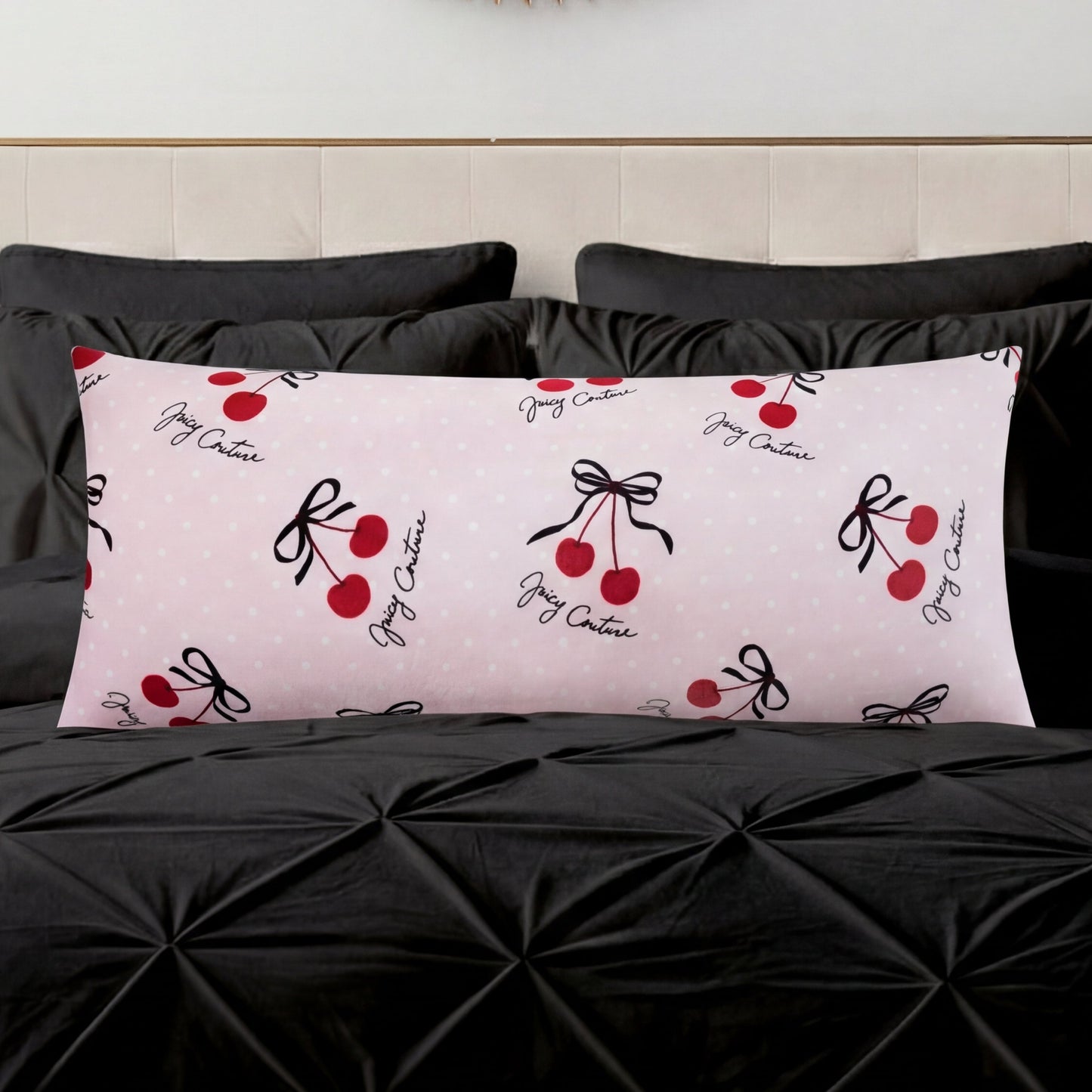 A Plush Body Pillow in light pink with red cherry and black bow designs and cursive text adds a chic pattern accent on a black tufted bedspread, set against a light-colored headboard.