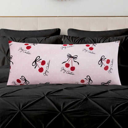 A Plush Body Pillow in light pink with red cherry and black bow designs and cursive text adds a chic pattern accent on a black tufted bedspread, set against a light-colored headboard.