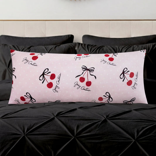A Plush Body Pillow in light pink with red cherry and black bow designs and cursive text adds a chic pattern accent on a black tufted bedspread, set against a light-colored headboard.