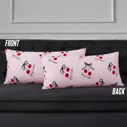 Two pink Plush Body Pillows with red cherries, black bows, and script branding add a chic touch. Labeled "FRONT" and "BACK," these oversized pillows rest on a dark gray couch.