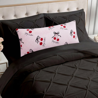 A bed with a black tufted comforter and matching pillowcases features the Plush Body Pillow—oversized, plush, and pink with red cherries, black bows, and cursive accents. The chic pattern pops against the beige tufted headboard.